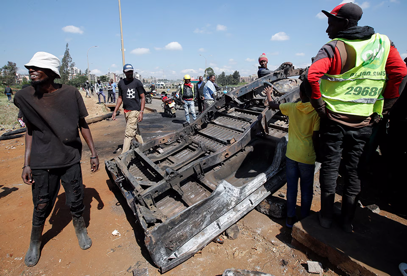 People stand next to a police vehicle that was burned during a demonstrations against the Kenya's proposed finance bill 2024/2025 in Nairobi, Kenya, June 26, 2024