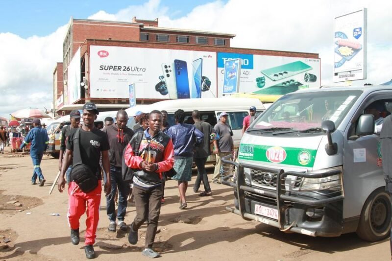 People are seen in front of parked public transport vehicles at a station in Harare, Zimbabwe, on March 11, 2026